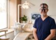 Confident dentist wearing loupes and scrubs in a bright modern dental operatory