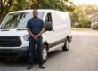 Plumbing business owner standing confidently in front of a clean white service van on a residential street